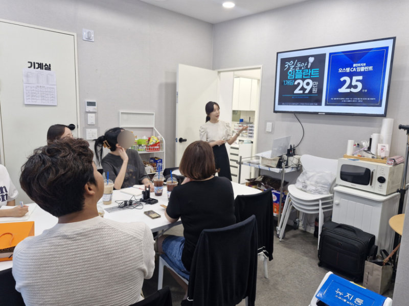 치과 컨설턴트가 여러 명의 수강생 앞에서 임플란트 관련 자료를 화면에 띄워 놓고 설명하는 모습